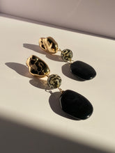 Black and gold statement drop earrings with sculptural gold tops, leopard-patterned round beads, and oversized glossy black oval drops