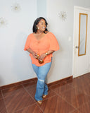 Plus size model smiling in coral blouse styled with fitted jeans and gold accessories