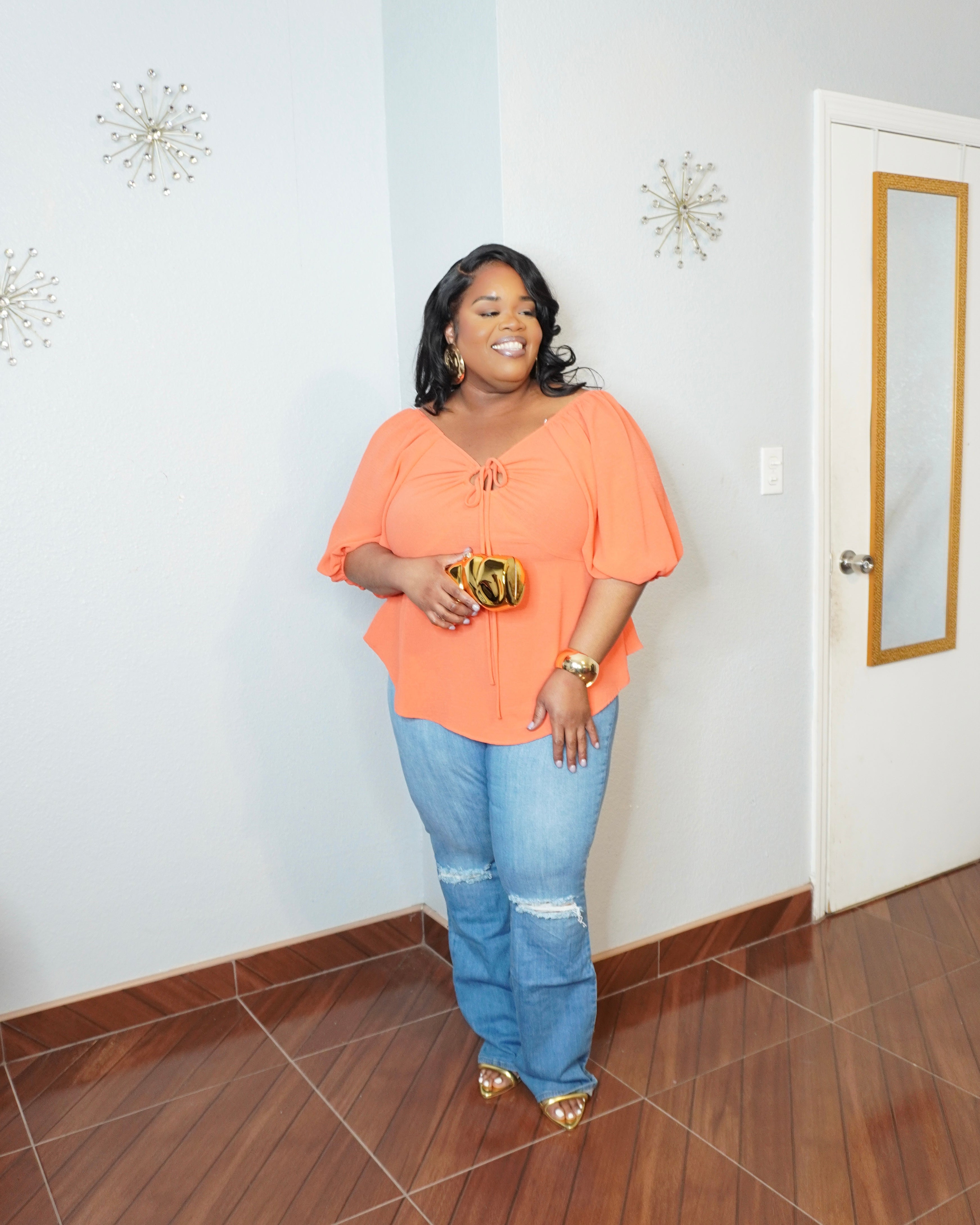 Plus size model wearing coral tie front blouse with puff sleeves and jeans front view