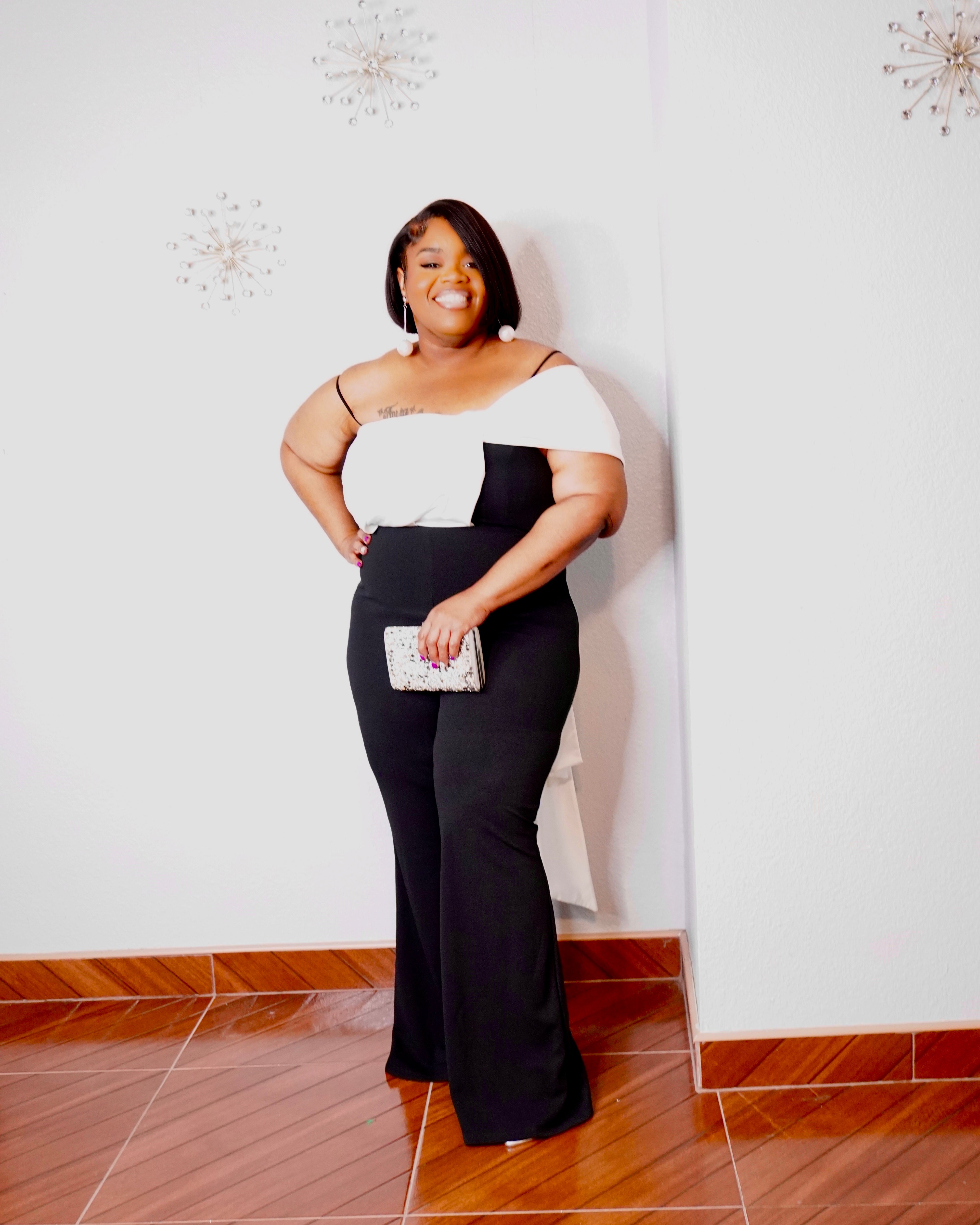 Elegant plus-size evening jumpsuit with asymmetrical white draping and flowing black wide-leg pants.