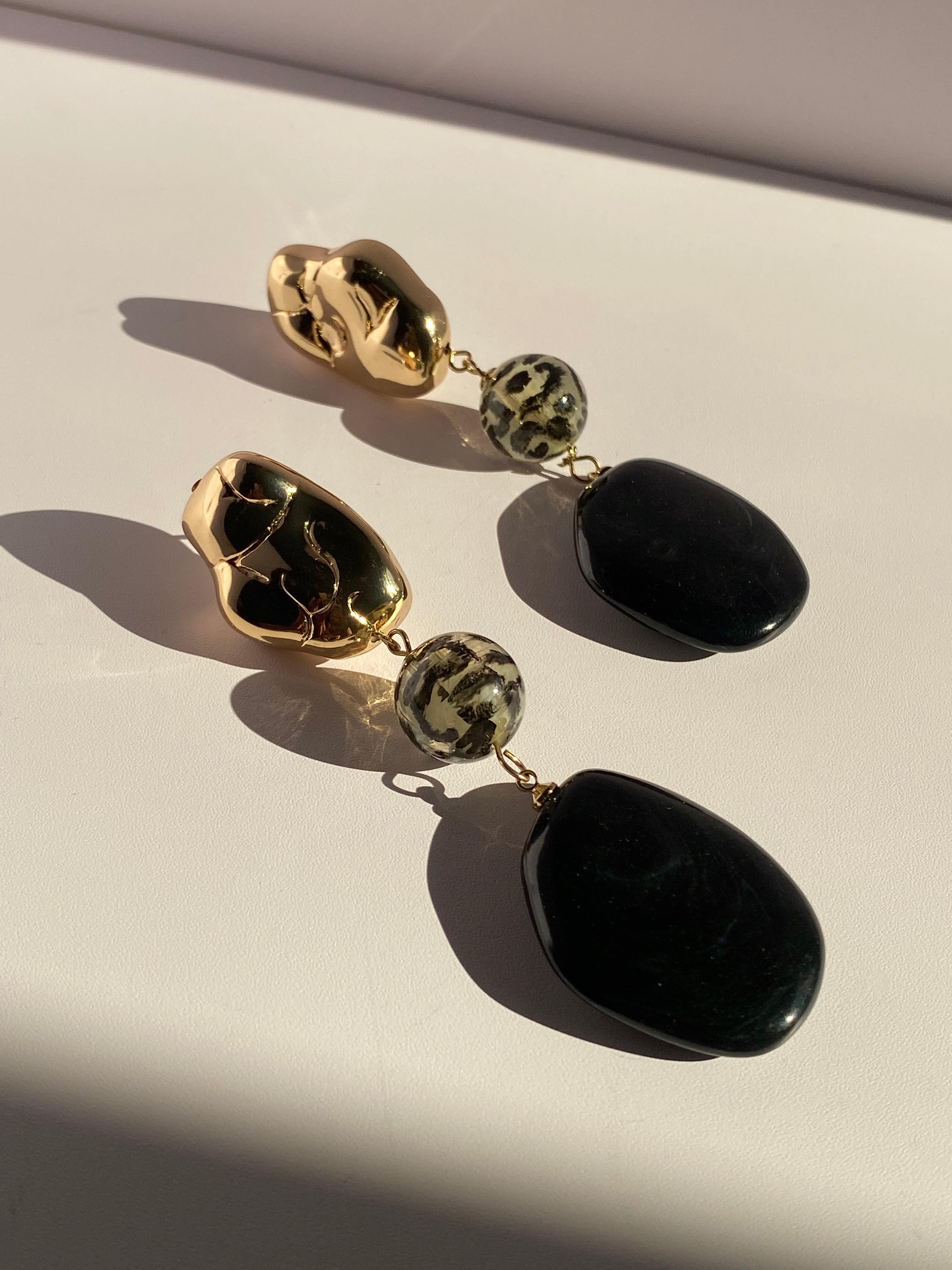 Oversized black and gold dangle earrings featuring polished gold accents, cream and black animal-print beads, and black oval pendants