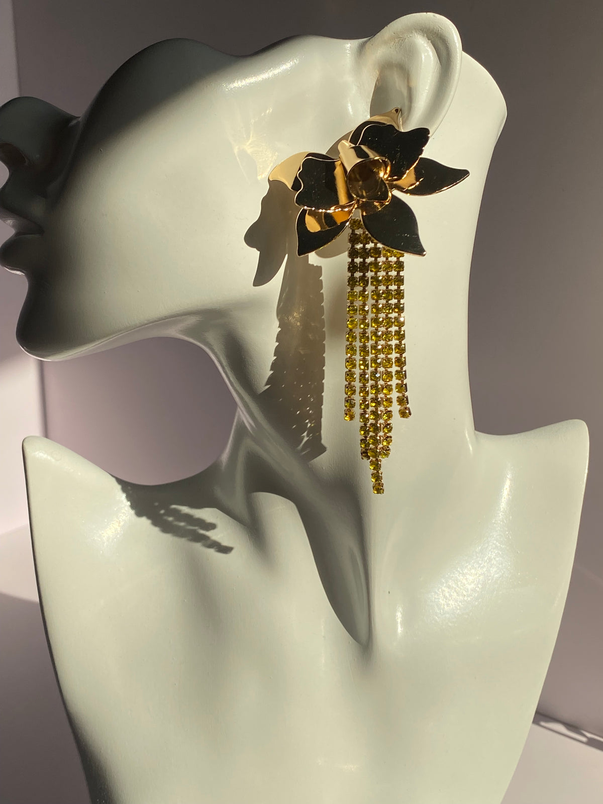 Gold flower statement earring featuring oversized sculptural metallic petals and cascading yellow rhinestone tassels