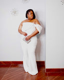 Plus size woman modeling the LYSAIRE Ivory Empress ivory-white formal jumpsuit, featuring an elegant strapless neckline, asymmetrical draped bodice, sparkling shoulder embellishment, dramatic off-shoulder sleeve, fitted waist, and flowing full-length wide-leg pants, accessorized with silver statement earrings and a sparkling crystal clutch for a sophisticated evening look.