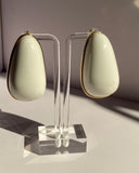 Elegant ivory teardrop stud earrings with gold-tone trim displayed on transparent jewelry stand