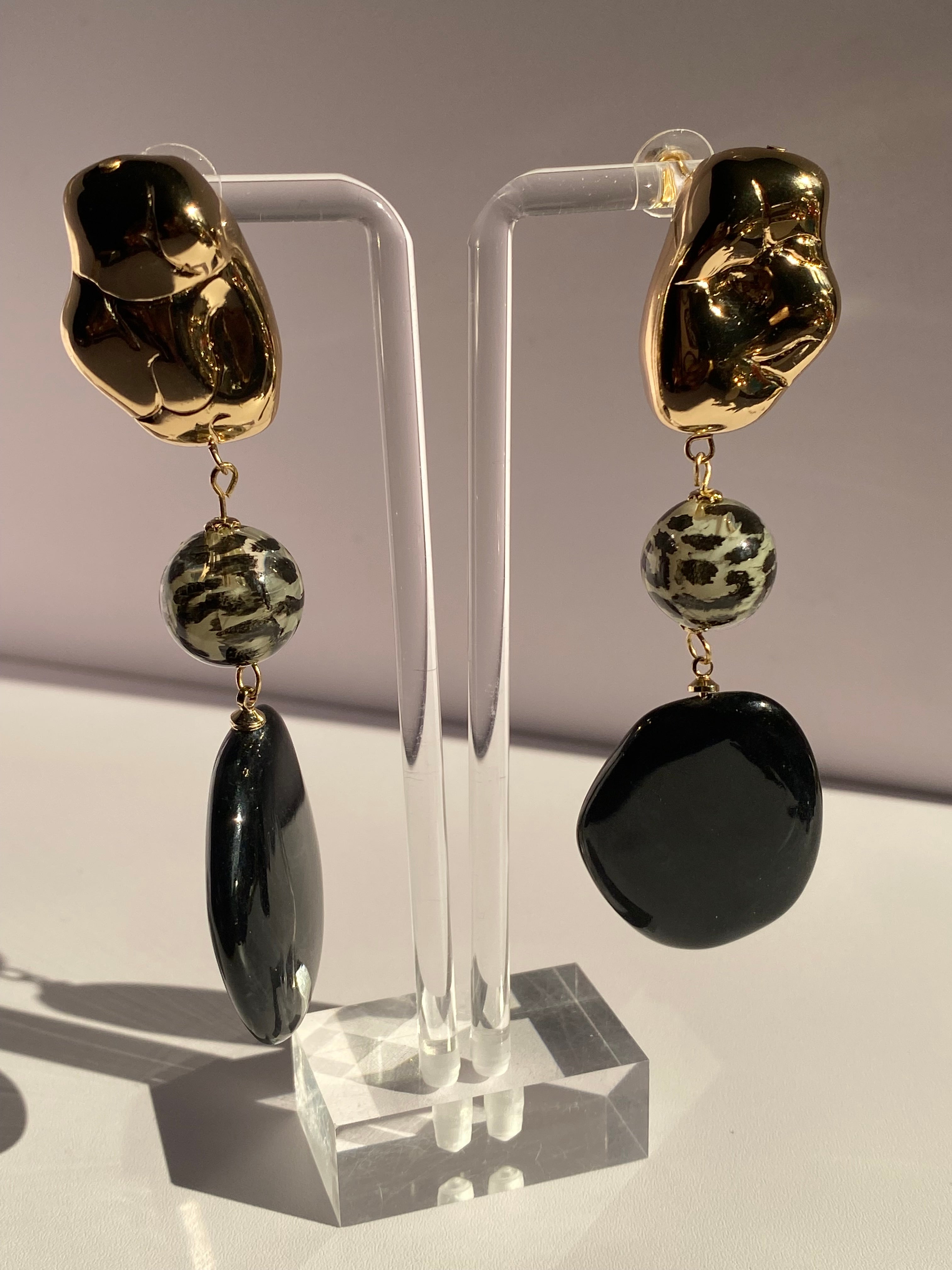 Long black statement earrings with sculptural gold-tone tops, leopard-print center beads, and glossy black oval drops displayed on jewelry stand